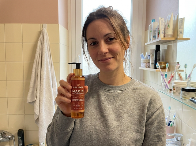 Femme tenant le flacon d'huile corps Relievu dans sa salle de bains